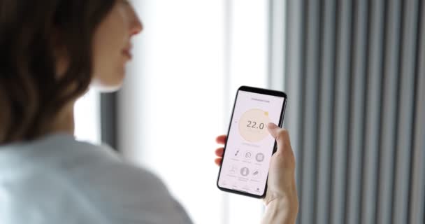 Mulher ajustando a temperatura ambiente com um telefone inteligente — Vídeo de Stock