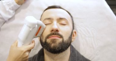 Kozmetik salonunda ultrason yüz kaldırma prosedürü uygulayan bir adam.