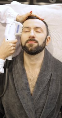 Kozmetik salonunda ultrason yüz kaldırma prosedürü uygulayan bir adam.