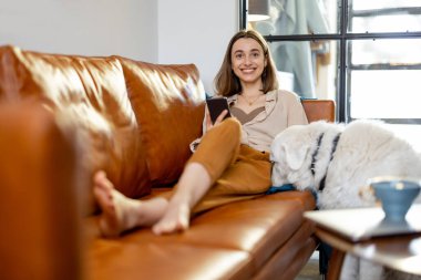 Evde bir köpekle kanepede oturan bir kadın..