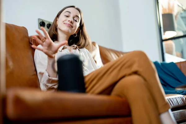 Woman speaking with audio assistant column on sofa