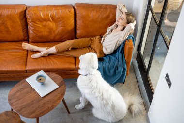 Evde bir köpekle kanepede oturan bir kadın..