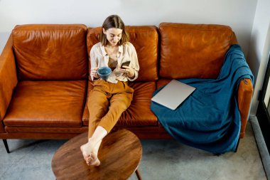 Evdeki kanepede oturan akıllı telefonlu kadın.