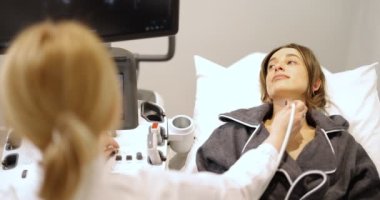 Doktor, klinikte ultrason taraması yapılan kadın hastanın tiroidini inceliyor.