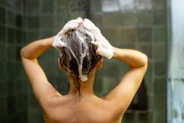 Duş alan kadın sıcak suyun altında dinleniyor.