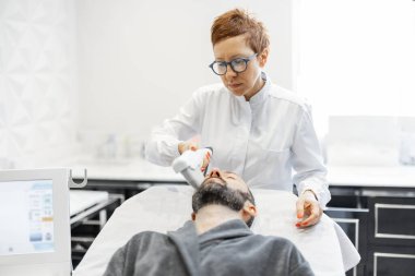 Kozmetik salonunda ultrason yüz kaldırma prosedürü uygulayan bir adam.