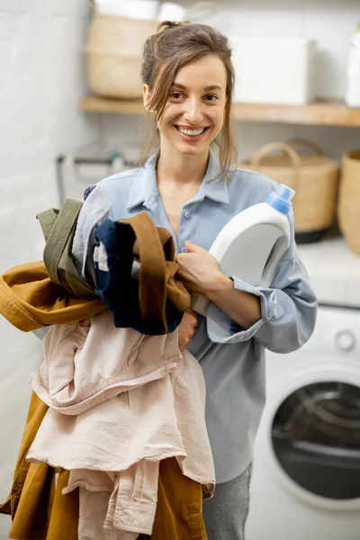 Femme avec des vêtements propres et détergent dans la buanderie à la maison — Photo