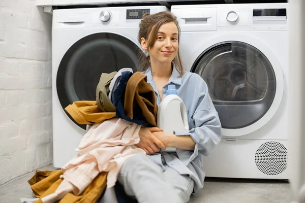 Femme avec des vêtements propres et détergent dans la buanderie à la maison — Photo