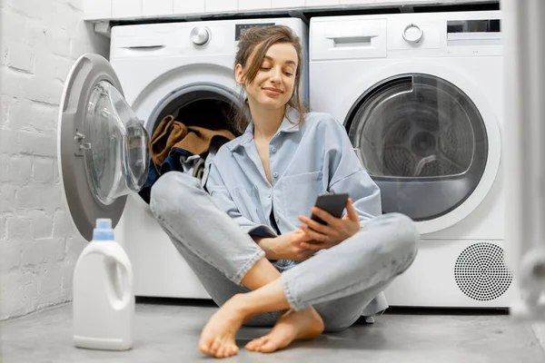 Avslappnad kvinna med en smartphone i tvättstugan — Stockfoto