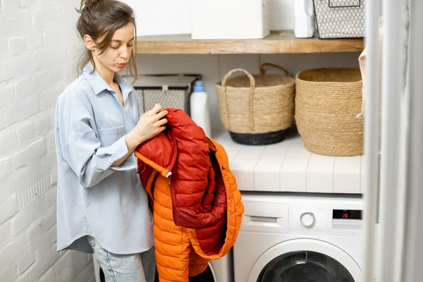 Young housewife looks on a down jacket before washing — Stock Photo, Image