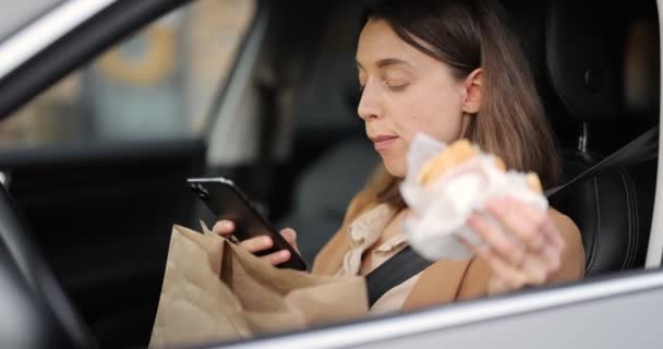 Mujer escribiendo en un teléfono inteligente mientras toma un aperitivo en un vehículo — Vídeos de Stock