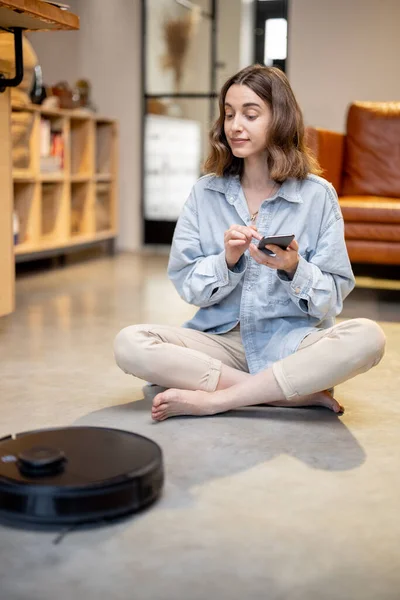 Avslappnad kvinna med telefon och robotdammsugare — Stockfoto