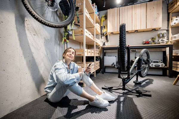 Praktisk kvinna med telefon och cykel i verkstaden hemma — Stockfoto
