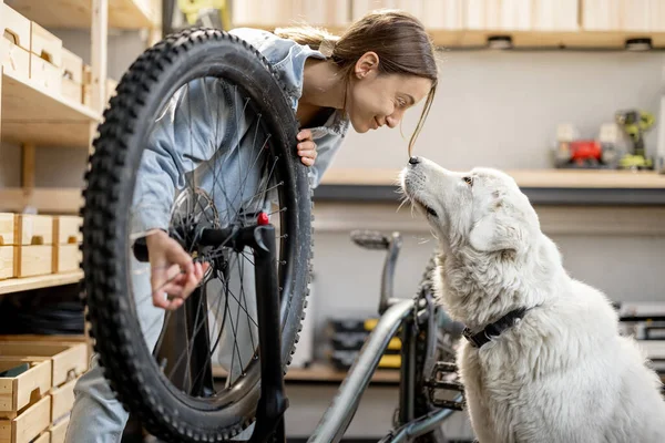 Praktisk kvinna med hund reparera cykel i verkstaden — Stockfoto