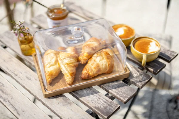 Croissants under the glass cloche with cups of coffee — Stock Photo, Image