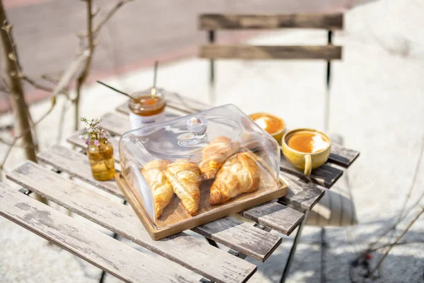Croissants under the glass cloche with cups of coffee — Stock Photo, Image