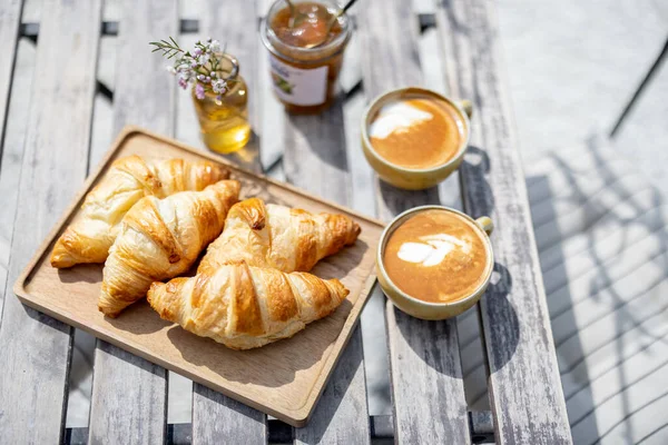 Croissants under the glass cloche with cups of coffee — Stock Photo, Image