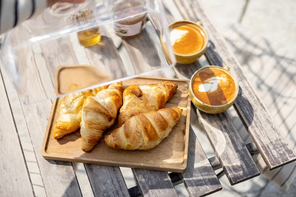 Croissants under the glass cloche with cups of coffee — Stock Photo, Image