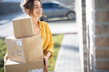 Evin önünde elinde paketler olan bir kadın.