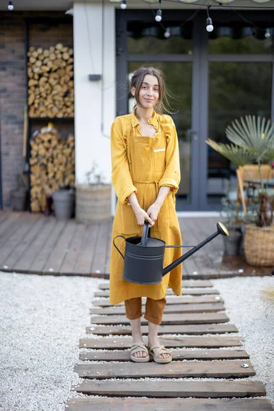 Dona de casa alegre no jardineiro avental amarelo cuida de plantas — Fotografia de Stock