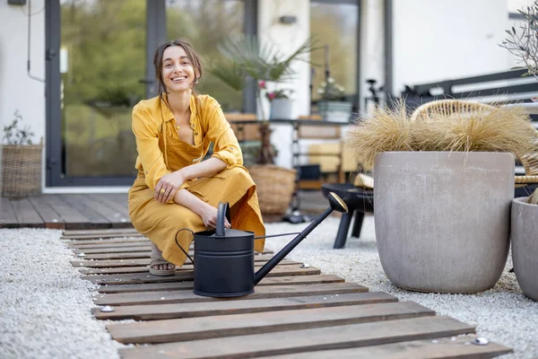 Dona de casa alegre no jardineiro avental amarelo cuida de plantas — Fotografia de Stock