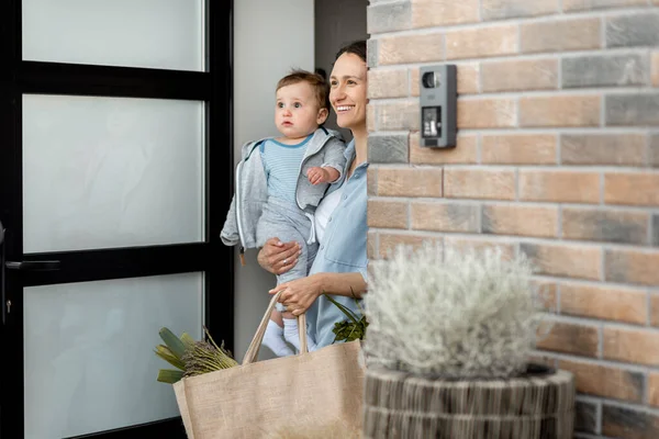 Šťastná hospodyňka s novorozeným synem, kteří stojí před dveřmi — Stock fotografie