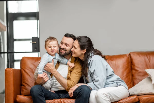 Pai feliz, mãe e filho pequeno estão brincando no sofá na sala de estar. Cuidados infantis e parentalidade — Fotografia de Stock