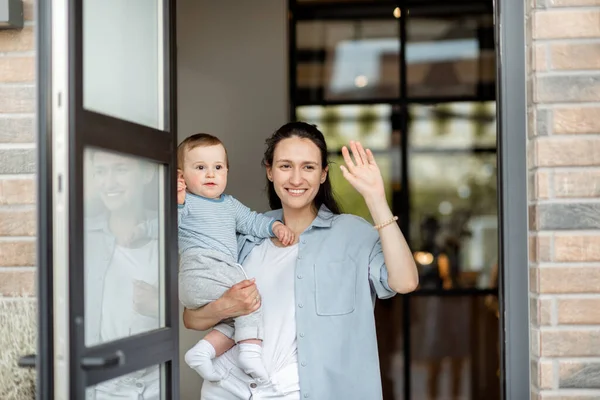 Housewife with newborn baby staying in front of entrance door