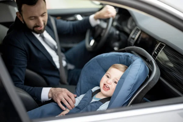 Isä ajaa töissä vauvan istuessa nykyaikaisella turvaistuimella.. — kuvapankkivalokuva