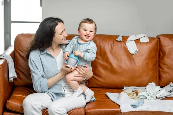 Ung mamma sitter med nyfödd son på soffan. — Stockfoto