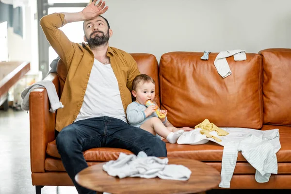 Müder Vater stillt ein Neugeborenes, während er auf dem Sofa sitzt — Stockfoto
