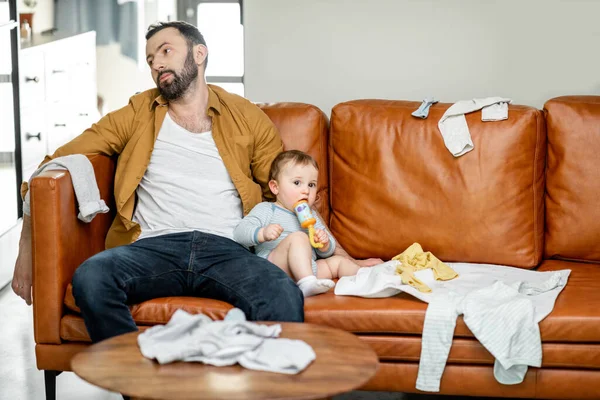Unavený otec kojit novorozence, zatímco sedí na pohovce — Stock fotografie