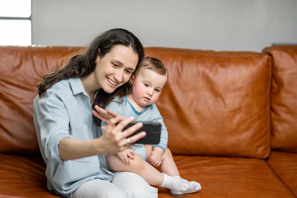 Ung mamma sitter med nyfödd son på soffan. — Stockfoto