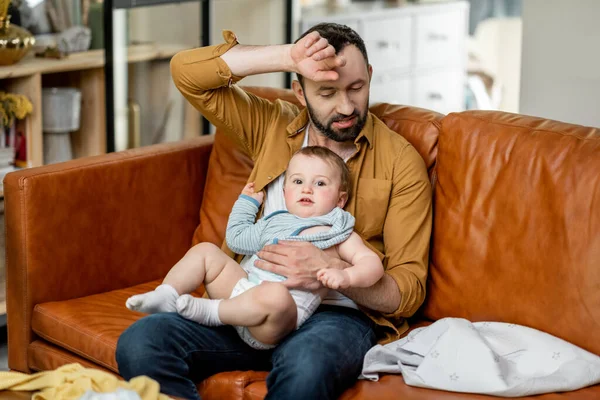 Unavený otec kojit novorozence, zatímco sedí na pohovce — Stock fotografie