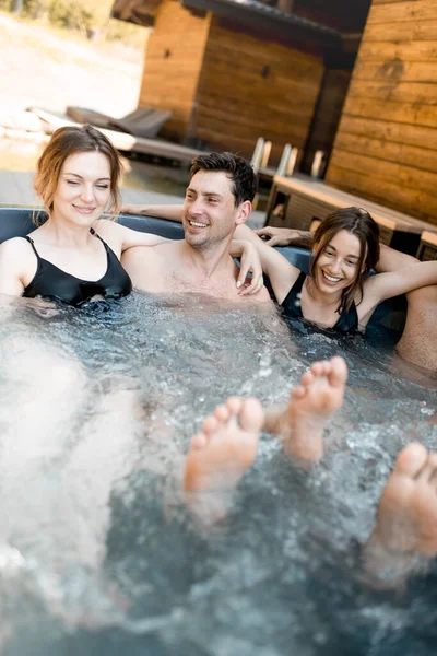 Компания друзей, парящихся в ванне на открытом воздухе возле спа-салона и озера — стоковое фото
