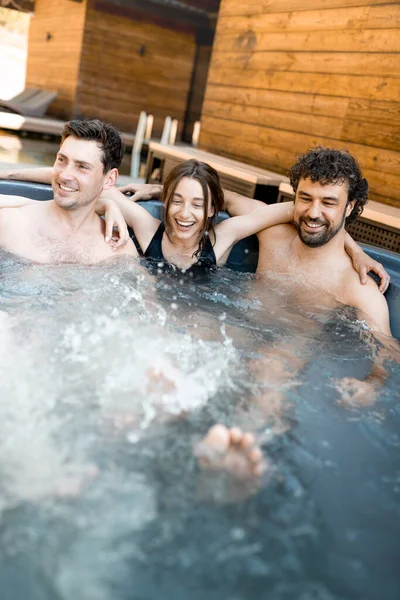 Compagnie d'amis vaporisant dans une baignoire en plein air près du spa et du lac — Photo