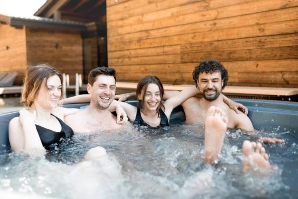 Compañía de amigos que humean en una bañera al aire libre cerca del spa y el lago —  Fotos de Stock