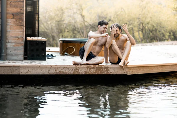 Companhia de amigos do sexo masculino sentados no terraço e molhando os pés — Fotografia de Stock