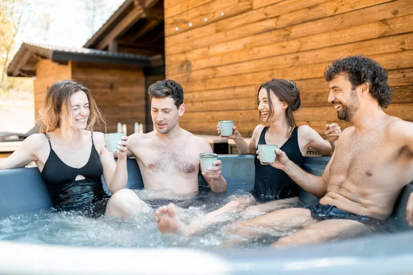 Compagnie d'amis vaporisant dans une baignoire en plein air près du spa et du lac — Photo