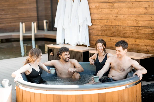 Company of friends steaming in a tub outdoors near the spa and lake
