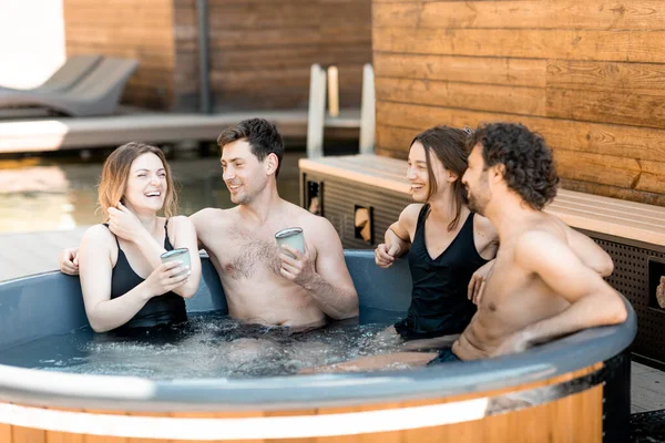 Compagnie d'amis vaporisant dans une baignoire en plein air près du spa et du lac — Photo