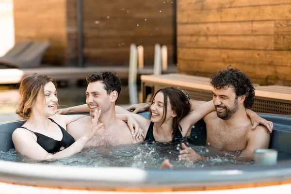 Compagnie d'amis vaporisant dans une baignoire en plein air près du spa et du lac — Photo