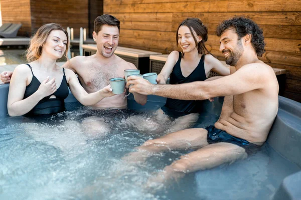 Compagnie d'amis vaporisant dans une baignoire en plein air près du spa et du lac — Photo