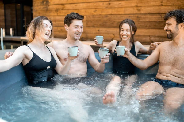 Compagnie d'amis vaporisant dans une baignoire en plein air près du spa et du lac — Photo