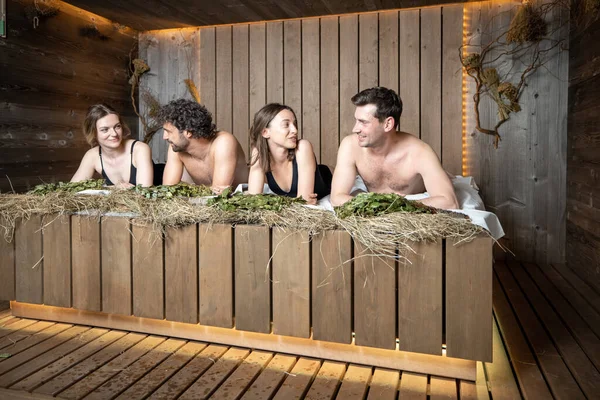 Compañía de amigos acostados en un banco de madera cubierto de heno — Foto de Stock