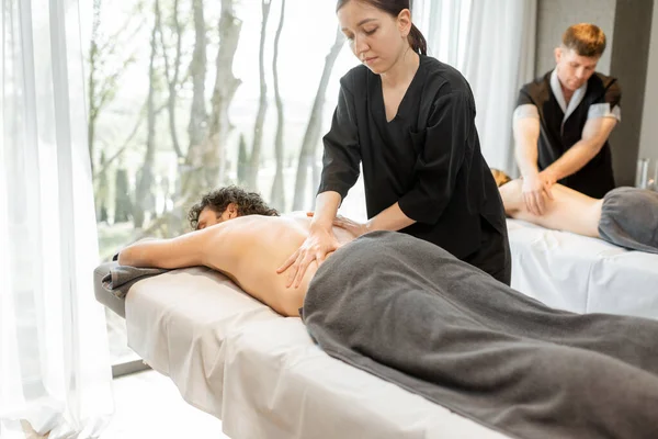 Beautiful couple lying in a spa salon enjoying getting deep back massage and relaxation. — Stock Photo, Image