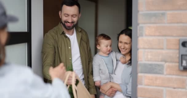 Kurier dostarcza zakupy młodej rodzinie w domu. — Wideo stockowe