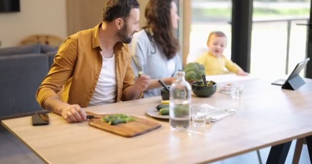 Νεαρή οικογένεια με ένα αγοράκι ενός έτους κατά τη διάρκεια του γεύματος στο σπίτι — Αρχείο Βίντεο