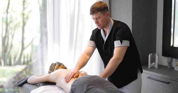 Мужской массажист делает расслабляющий массаж спины для молодой женщины — стоковое видео