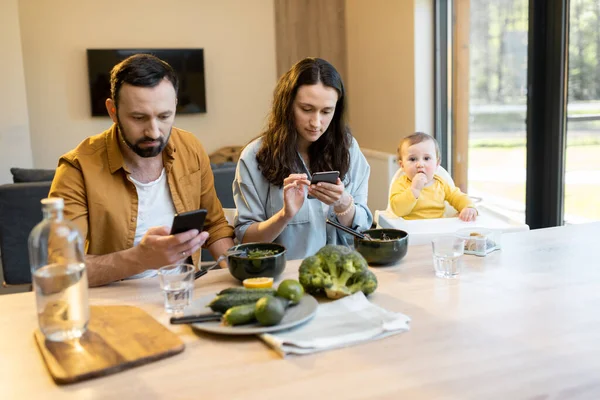 Eltern während eines Mittagessens mit ihrem kleinen Sohn mit ihren Telefonen beschäftigt — Stockfoto